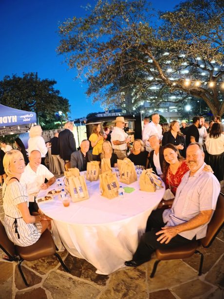 Top Shelf night: guests around a linen table at blue hour, vendor tents behind